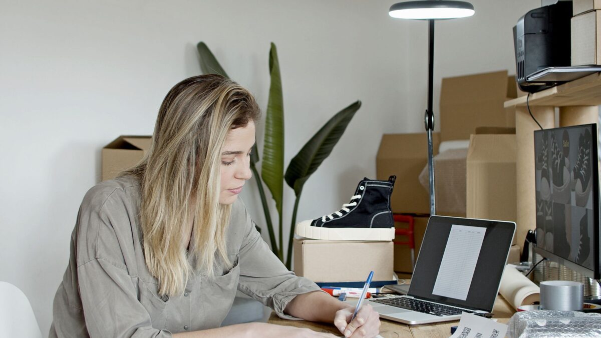 Businesswoman writing notes in a busy online store office in Portugal, focusing on growth and efficiency.