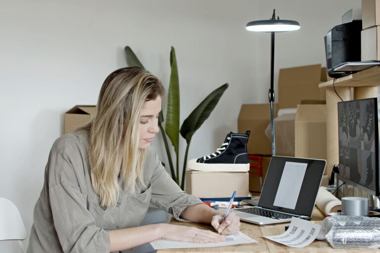 Businesswoman writing notes in a busy online store office in Portugal, focusing on growth and efficiency.