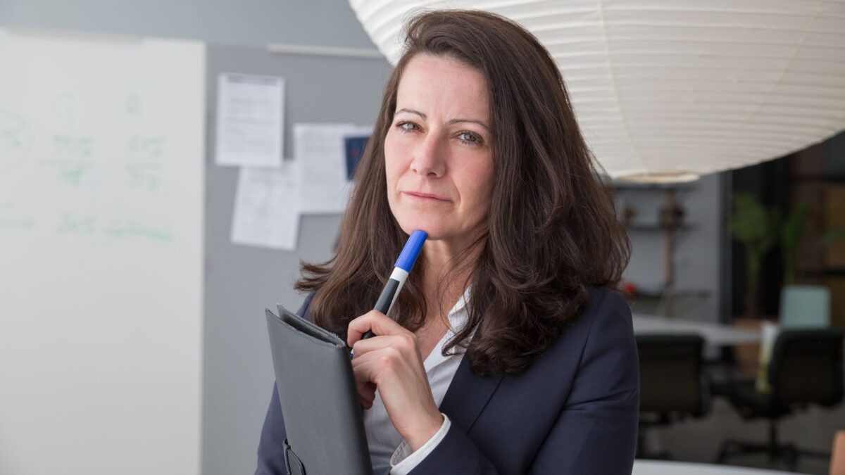 Businesswoman in corporate attire posing with a pen in a modern office setting.