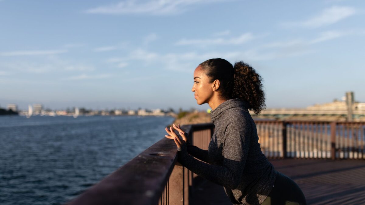 Black woman exercising on a wooden dock by the water during sunrise with a focused expression.
