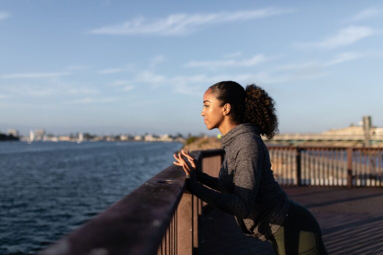 Black woman exercising on a wooden dock by the water during sunrise with a focused expression.