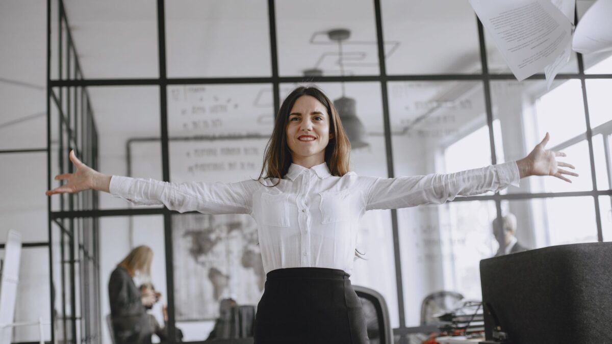 Smiling woman with arms open wide in a modern office environment.