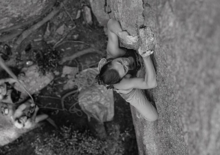 Dynamic black and white photo of a woman rock climbing on a steep outdoor surface.