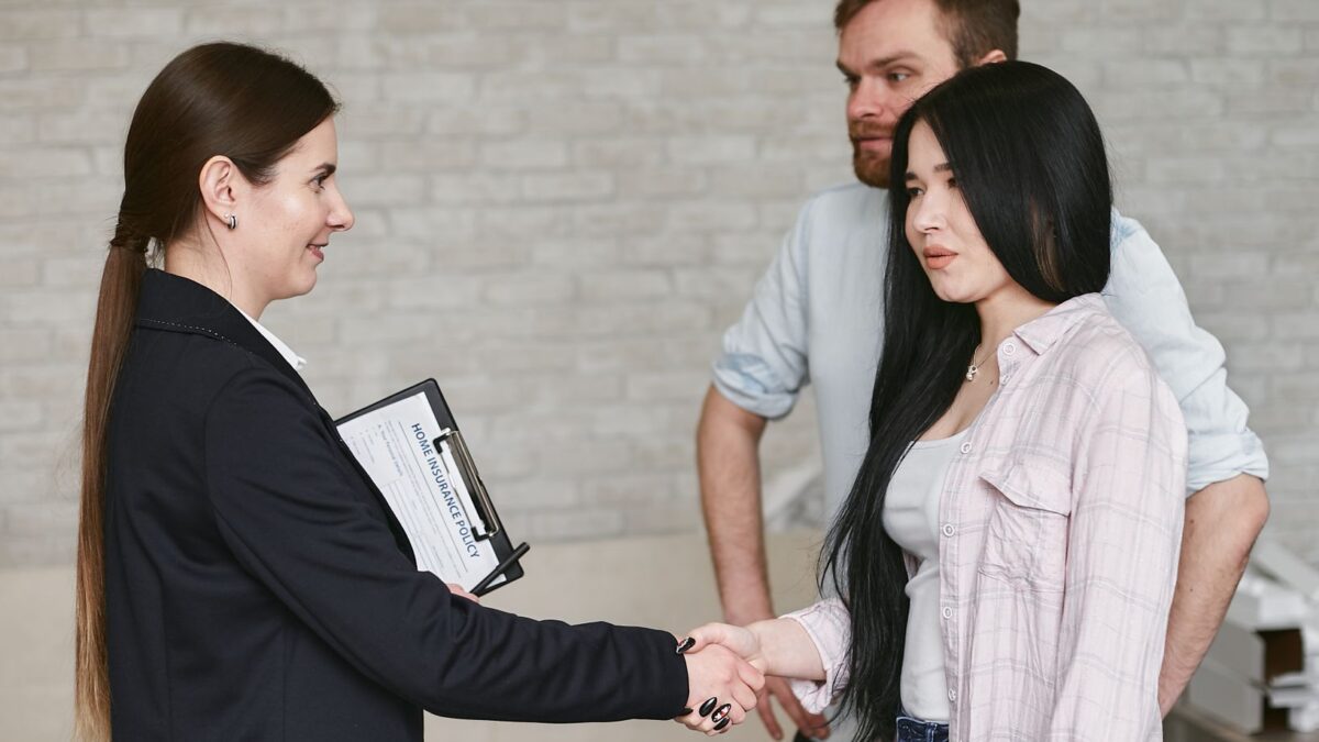 Professional business meeting with a handshake in an office environment featuring three adults in conversation.