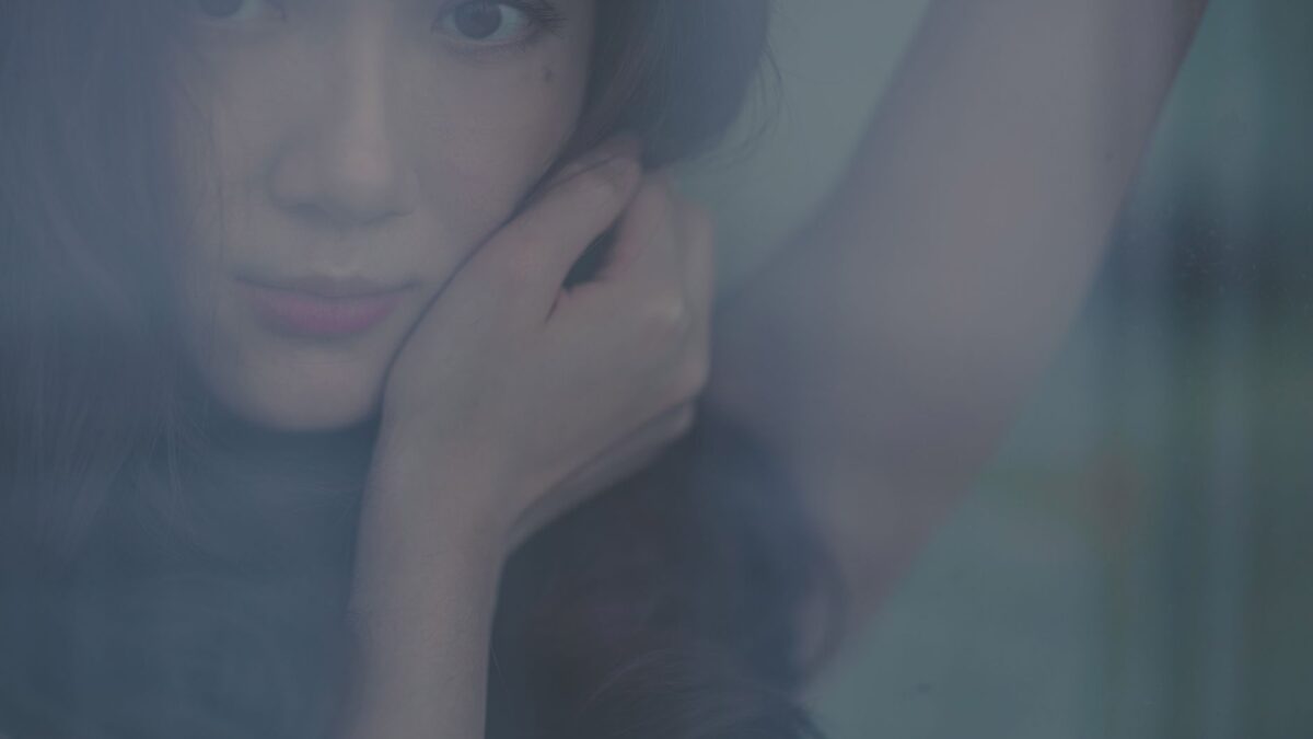 Artistic portrait of a young woman gazing through a window with a thoughtful expression.