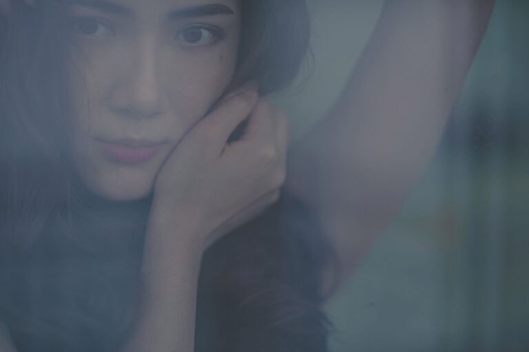 Artistic portrait of a young woman gazing through a window with a thoughtful expression.